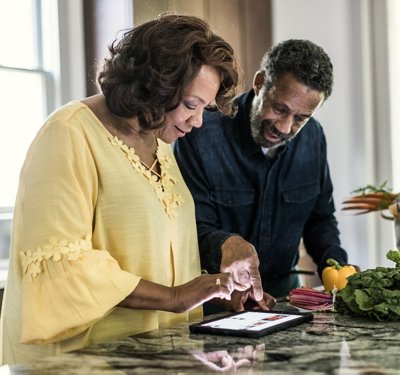 man and woman smiling in their kitchen while looking at a tablet screen